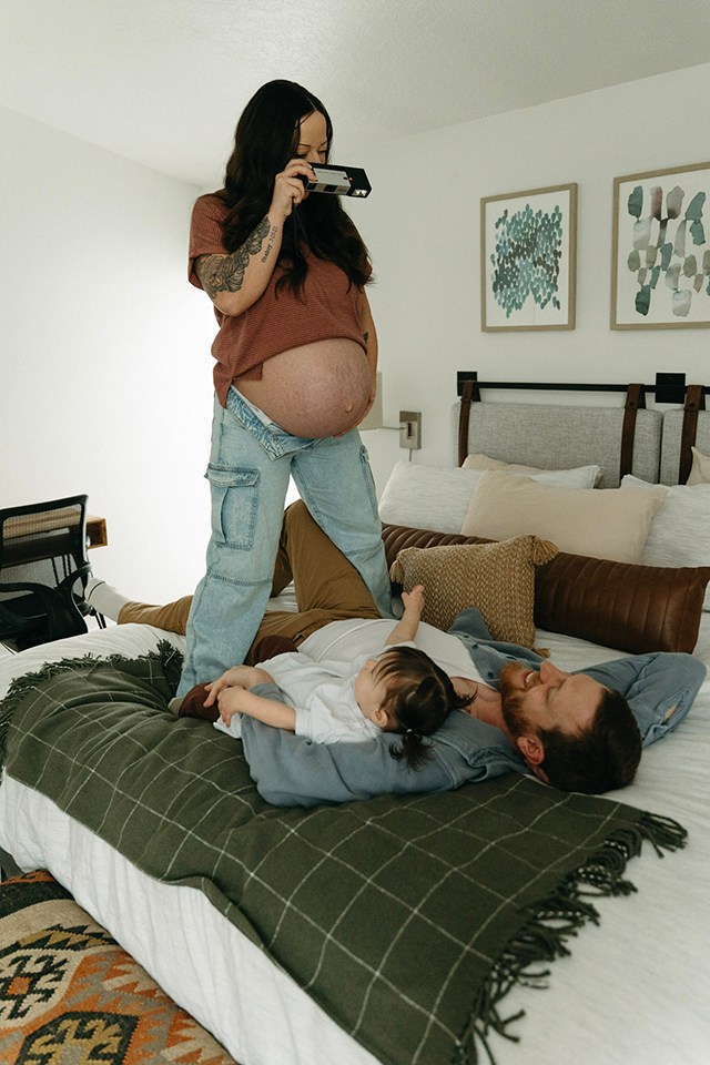 a pregnant woman standing and taking a photo of her husband and toddler, one of the best faceless photo ideas