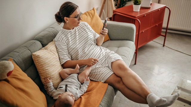 A mom with her baby beside her on the couch looking at private photo sharing apps